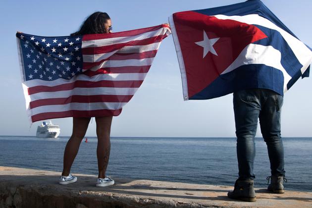 FILE - In this May 2, 2016 file photo, Yaney Cajigal, left, holds out a Stars and Stripes, and Dalwin Valdes holds a Cuban national flag, as they watch the arrival of Carnival's Adonia cruise ship from Miami, in Havana, Cuba, the first step toward a futur