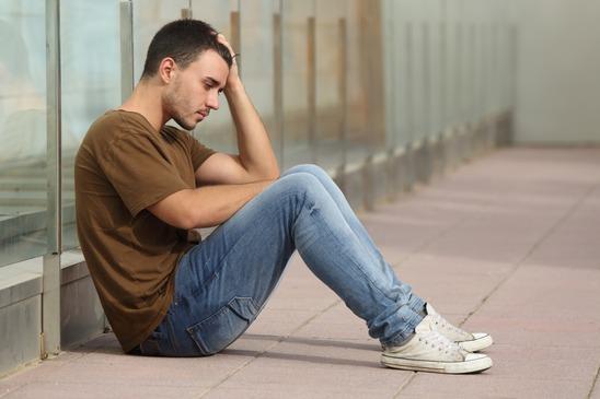 Teenager boy worried sitting on the floor with a hand on the head