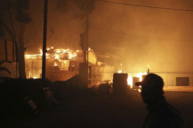 A person looks across at burning houses in the town of Mati, east of Athens, Monday, July 23, 2018. Regional authorities have declared a state of emergency in the eastern and western parts of the greater Athens area as fires fanned by gale-force winds rag