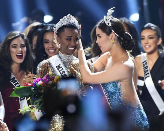 ATLANTA, GEORGIA - DECEMBER 08: (EDITORIAL USE ONLY) Miss Universe 2019 Zozibini Tunzi, of South Africa, is crowned onstage by Miss Universe 2018 Catriona Gray (R, in blue) at the 2019 Miss Universe Pageant at Tyler Perry Studios on December 08, 2019 in A